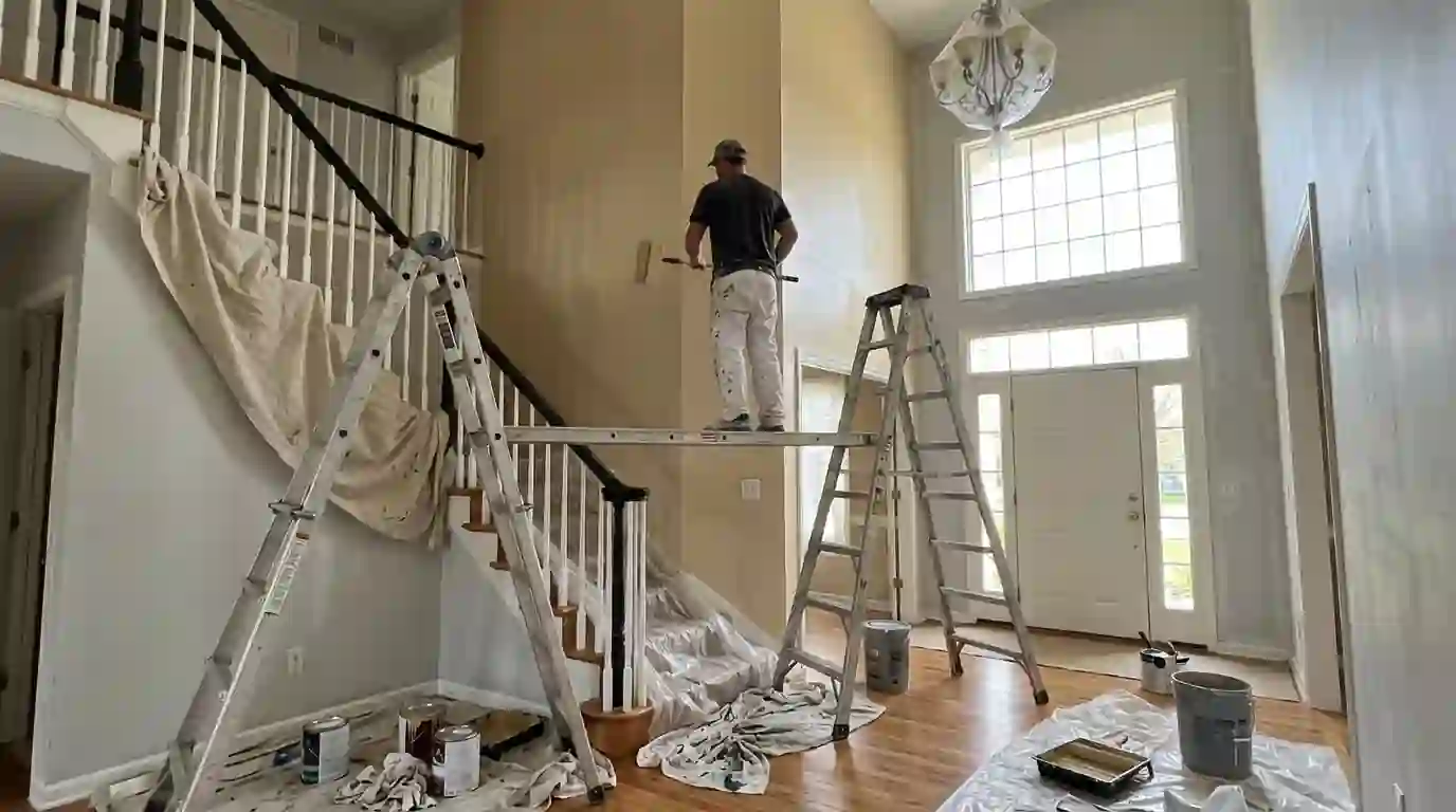 Painter on a plank rolling a two-story foyer wall